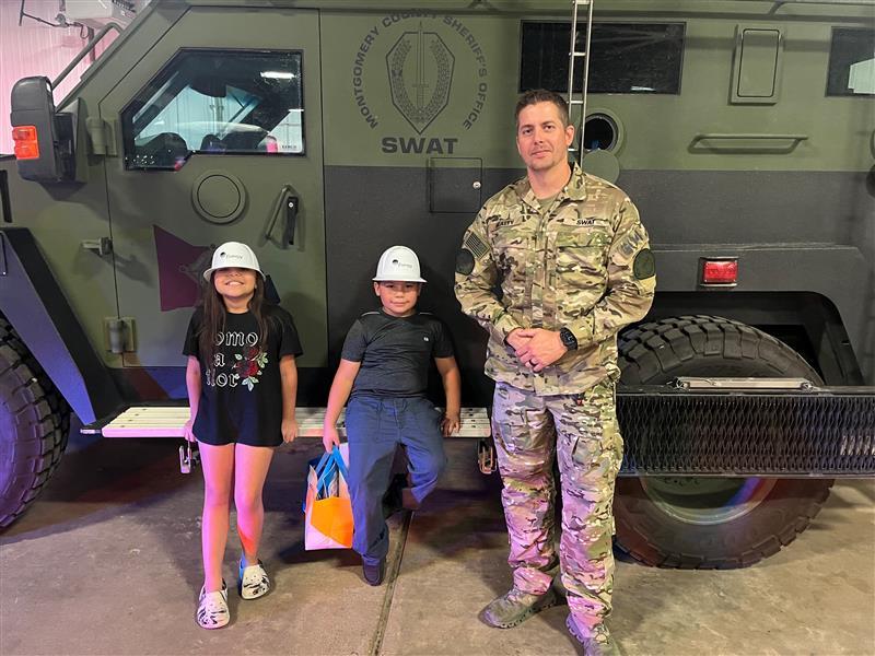 Photo at OBE with a Sheriff's Office SWAT member and two young children standing in front of a SWAT vehicle.